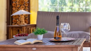 Ein Holztisch mit einer Flasche Akenta-Wein, einem Weinglas, einer Schale mit Kirschen, einer Topfpflanze und einem offenen Buch.