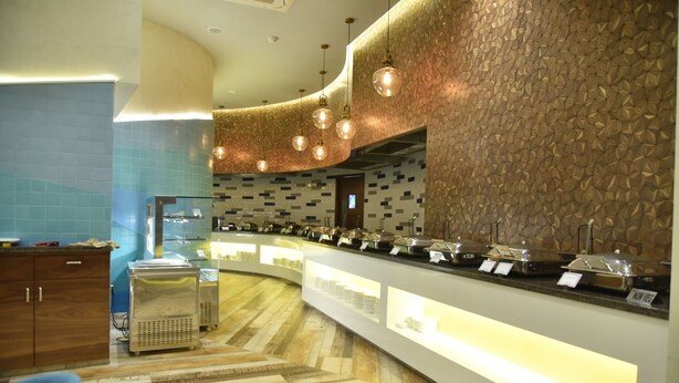 A buffet area with a curved counter, various food containers, and a patterned wall. - Effotel By Sayaji Vadodara (Vadodara)