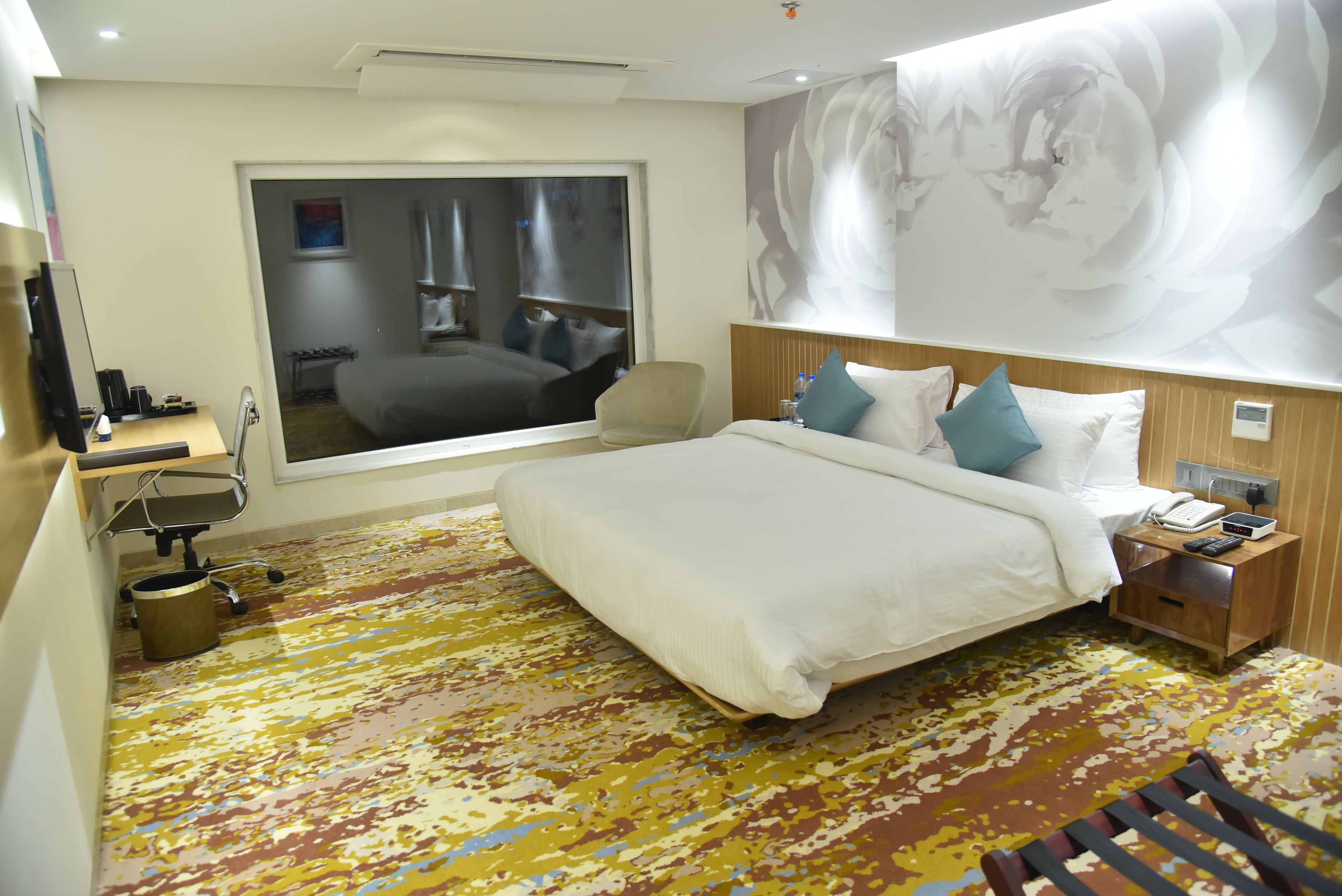 A hotel room with a large bed, a desk with a chair, a window with a view, and a wall-mounted phone.