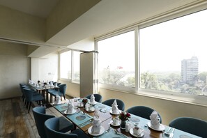 A dining area with tables set for six, large windows, and a view of a cityscape. - Effotel By Sayaji Vadodara (Vadodara)