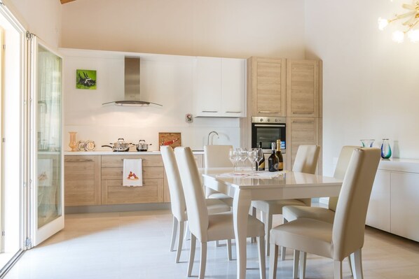 Une cuisine moderne avec des meubles blancs, une table à manger avec des chaises et un four encastré.