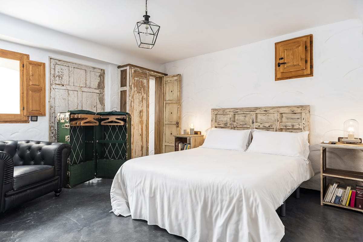 Une chambre à coucher avec un grand lit, un canapé en cuir, une armoire en bois et une valise verte.
