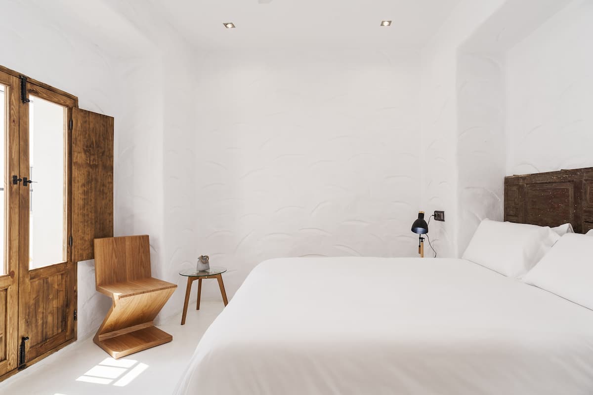 Une chambre à coucher avec un grand lit, une chaise en bois, une petite table et une lampe.