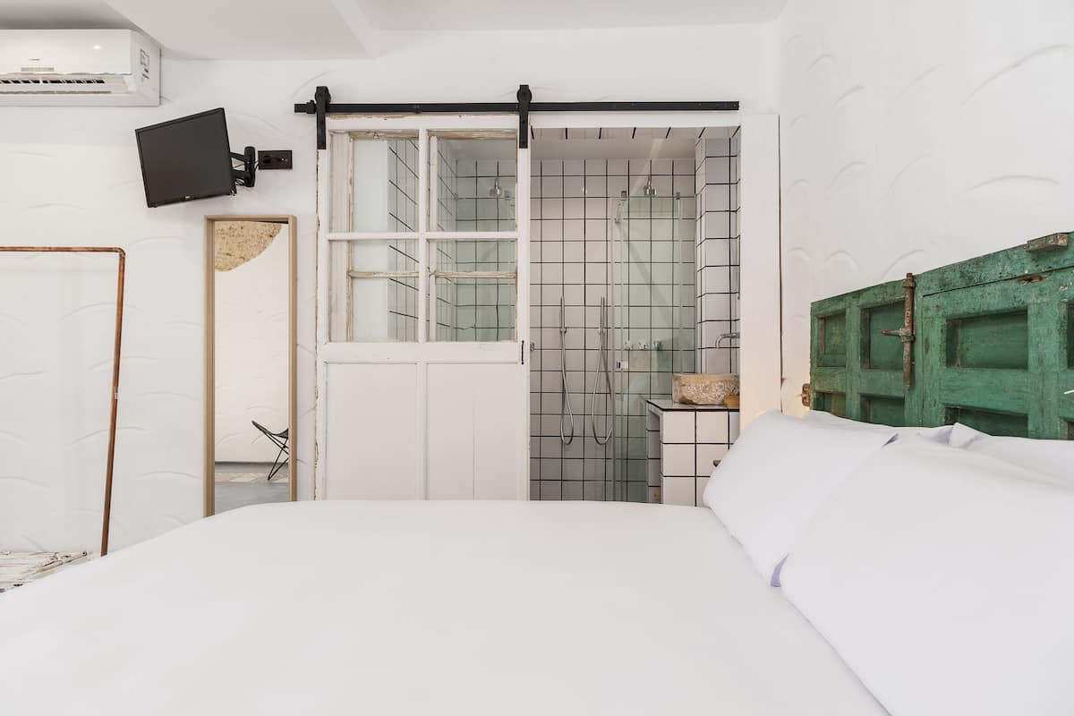 Une chambre avec un lit, une porte coulissante donnant sur une salle de bain, un téléviseur fixé au mur et une porte verte.