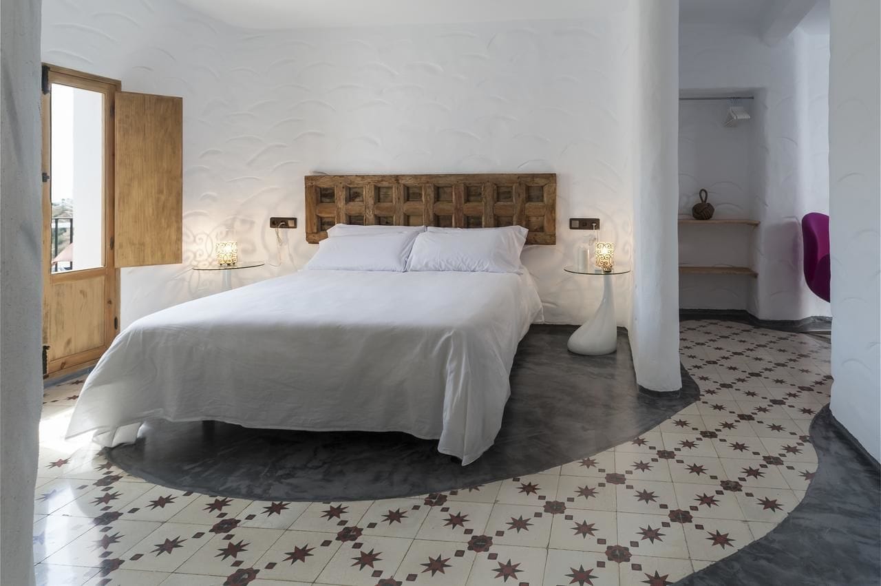 Un dormitorio con una cama grande, un cabecero de madera, dos mesitas de noche con lámparas y un suelo estampado.