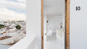 Une pièce aux murs blancs, dotée d’une porte en bois portant le numéro 10, qui donne sur une salle de bain moderne avec un lavabo blanc et un lit recouvert de linge de lit blanc.