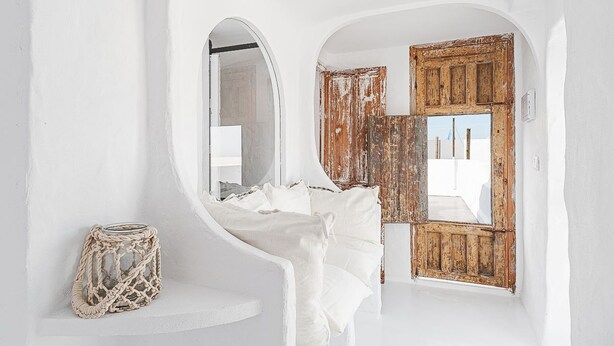 Une pièce blanche avec un lit, une porte en bois et une petite fenêtre.