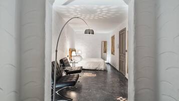 A modern hotel room with a black leather sofa, a small round table, a lamp, a bed, and a large mirror.