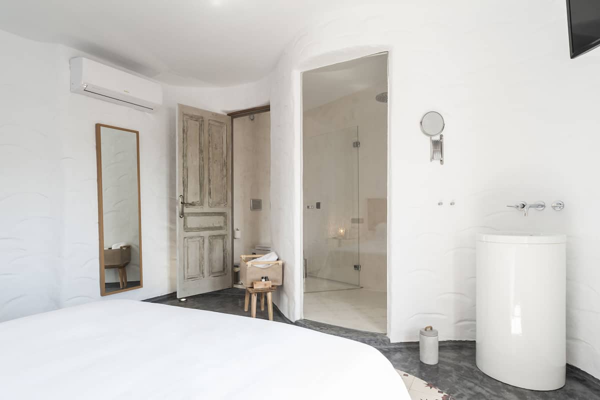 Une chambre à coucher moderne avec un grand lit, une porte en bois, une douche en verre et un lavabo blanc.