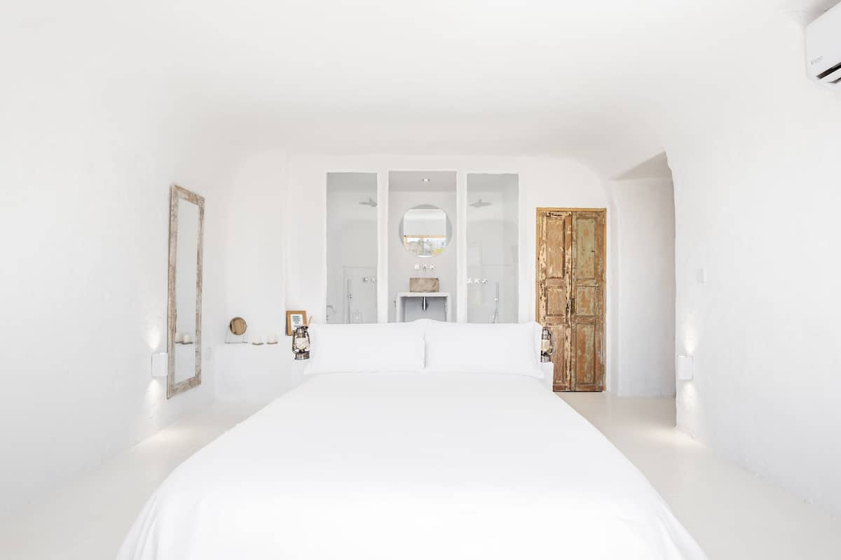 Une chambre à coucher au style minimaliste, avec un grand lit, une armoire en bois et une salle de bain visible à travers une cloison en verre.