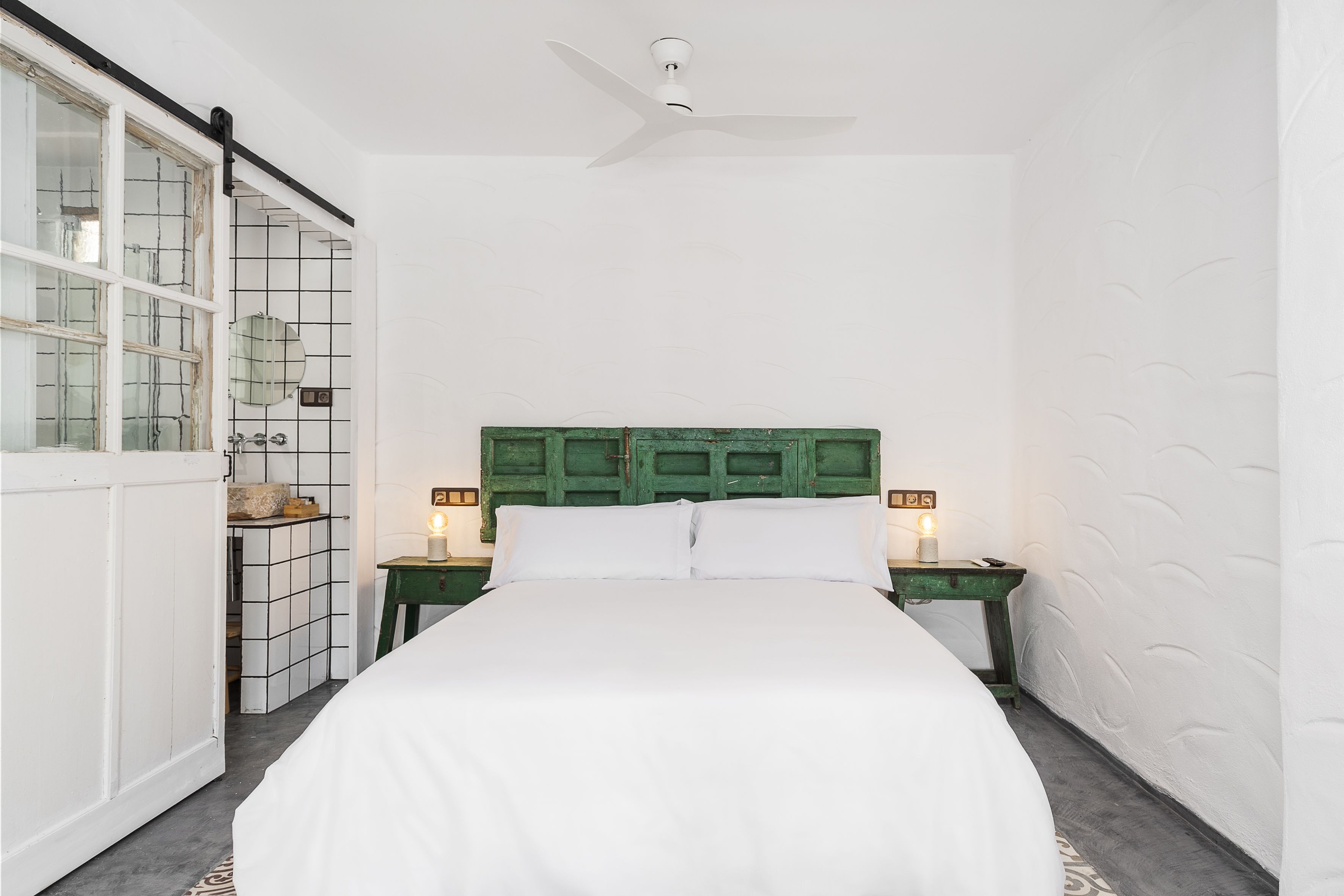 A bedroom with a bed, a green headboard, two bedside tables with lamps, and a ceiling fan.