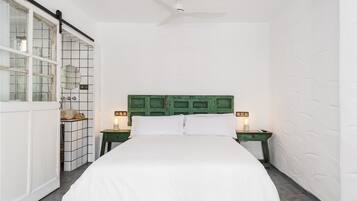 A bedroom with a bed, a green headboard, two bedside tables with lamps, and a ceiling fan.