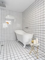 A bathroom with a white bathtub, a round mirror, and a small table with candles.