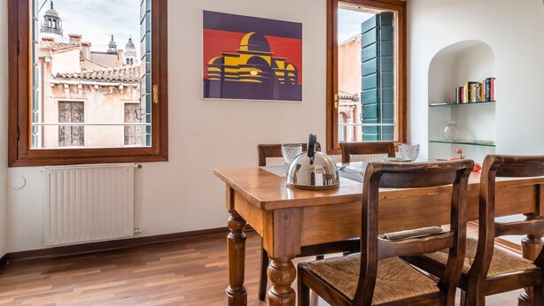 Un coin repas avec une table et des chaises en bois, un radiateur et une vue sur les bâtiments par une fenêtre.