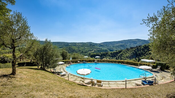 Une piscine avec vue sur les collines, entourée de chaises longues et de parasols.