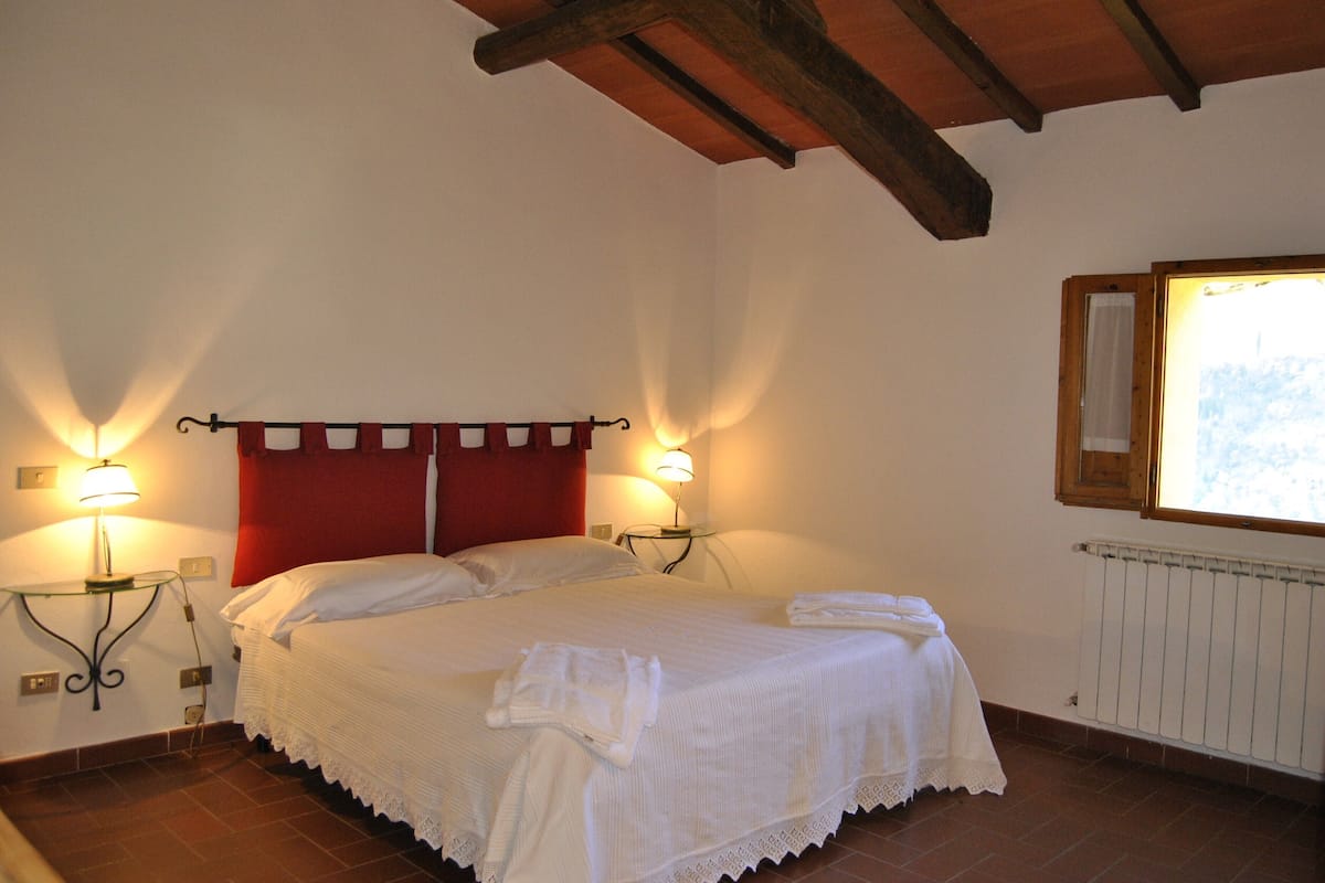 Een slaapkamer met een bed, twee bedlampen, een raam met uitzicht en een radiator.
