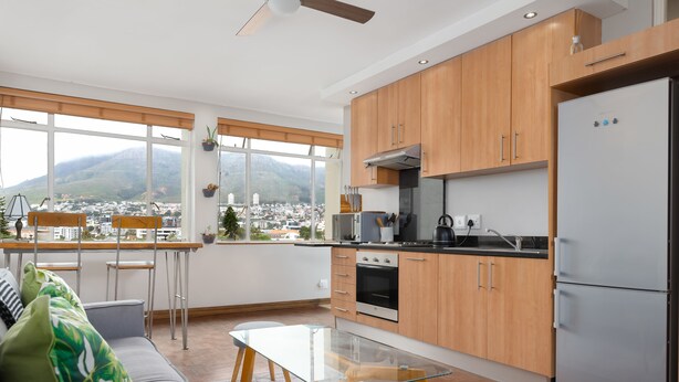 A modern kitchen with wooden cabinets, a stainless steel refrigerator, and a view of a city and mountains. - 66 Keerom 715 (Cape Town)
