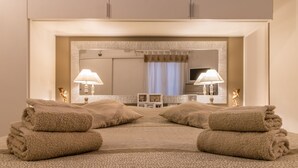 Habitación de hotel con un espejo grande, dos lámparas de noche, una cama con colcha estampada y dos toallas en el suelo.