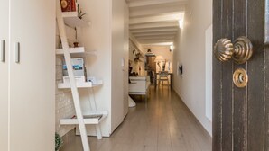 Un pasillo estrecho con una puerta de madera a la derecha, una estantería blanca a la izquierda y una silla blanca en el centro.