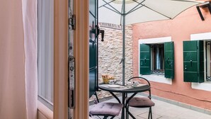 Un patio al aire libre con una mesa y sillas, una cesta de mimbre y una puerta con la etiqueta 'DISTACCA'.