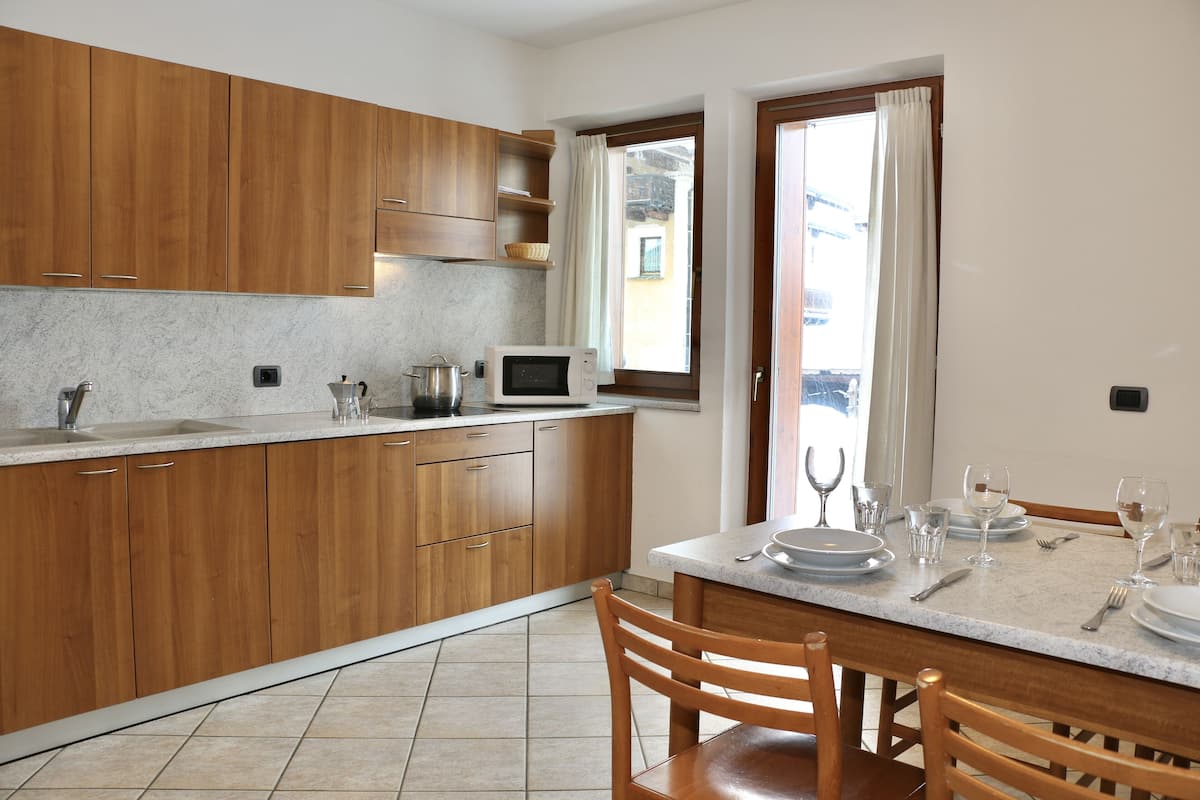 A kitchen with wooden cabinets, a microwave, and a dining table set for two with plates, glasses, and cutlery.