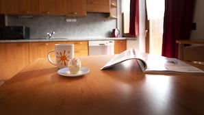A wooden table with a white mug and a cupcake, and an open magazine. - Appartamenti Brunnlein (Livigno)