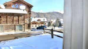 A rustic wooden building with a snow-covered roof, a wooden fence, and a mountain backdrop. - Appartamenti Brunnlein (Livigno)