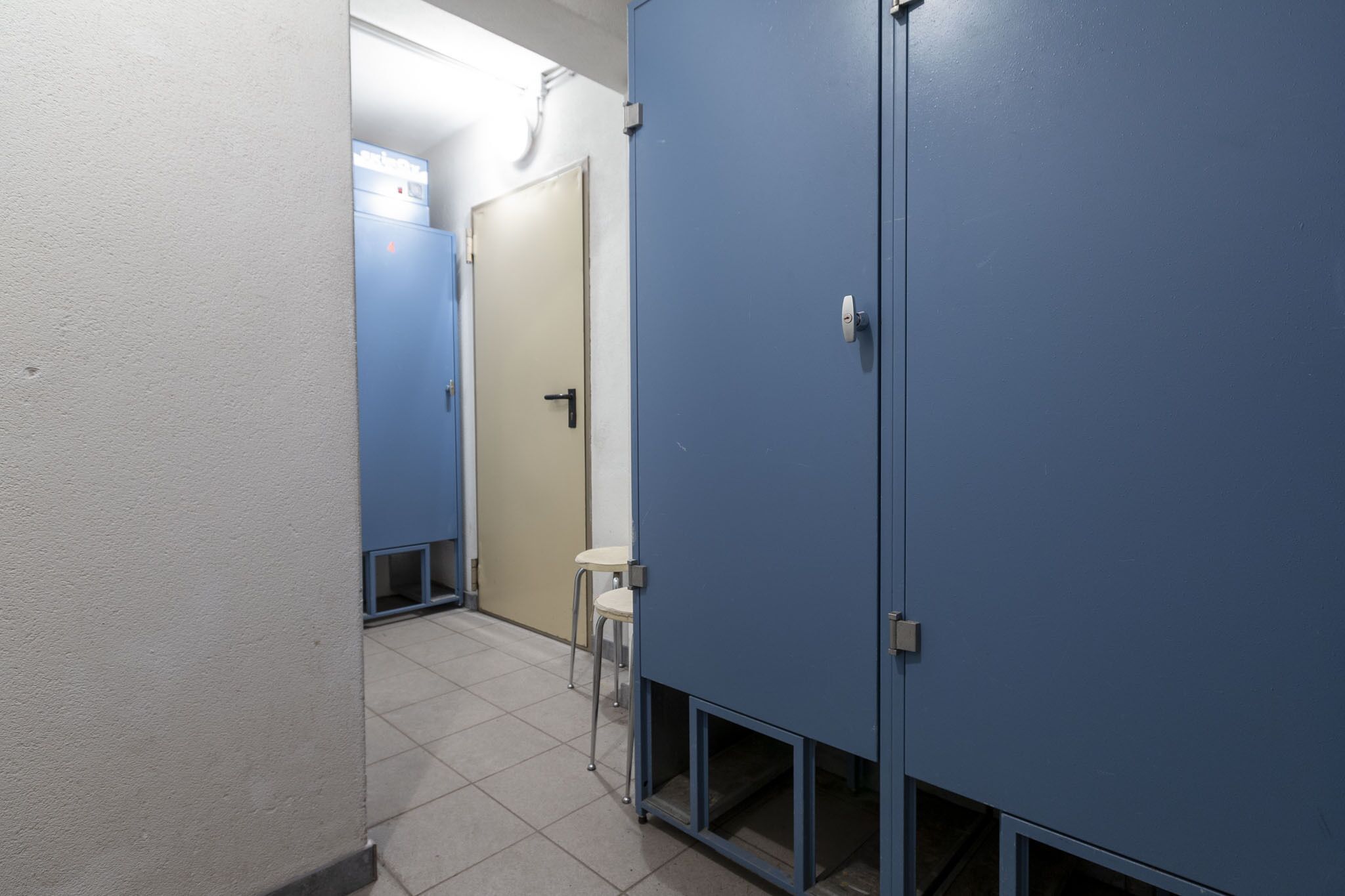 A hallway with blue lockers, a white wall, and a door leading to another room.