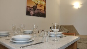 A dining table set with plates, glasses, and cutlery, a painting of a deer on the wall, and a sofa in the background. - Appartamenti Brunnlein (Livigno)