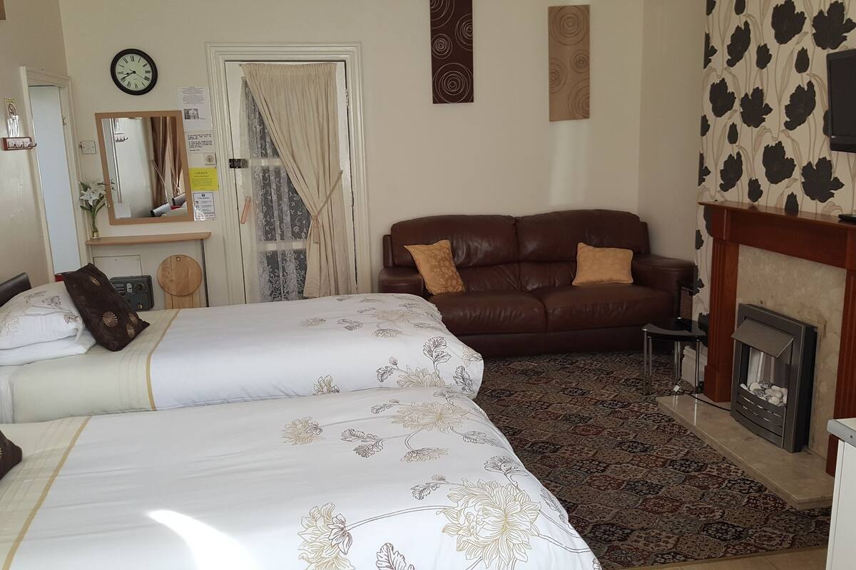 A bedroom with two beds, a brown leather sofa, a fireplace, and a television mounted on the wall.