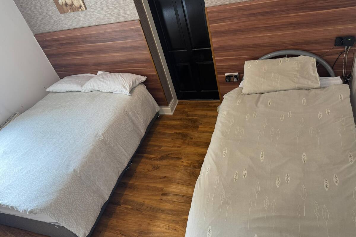A room with two beds, wooden flooring, a door, and a wall-mounted power outlet.