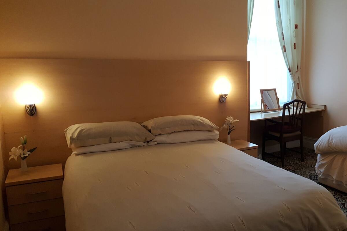 A hotel room with two beds, a desk, a chair, and a mirror.