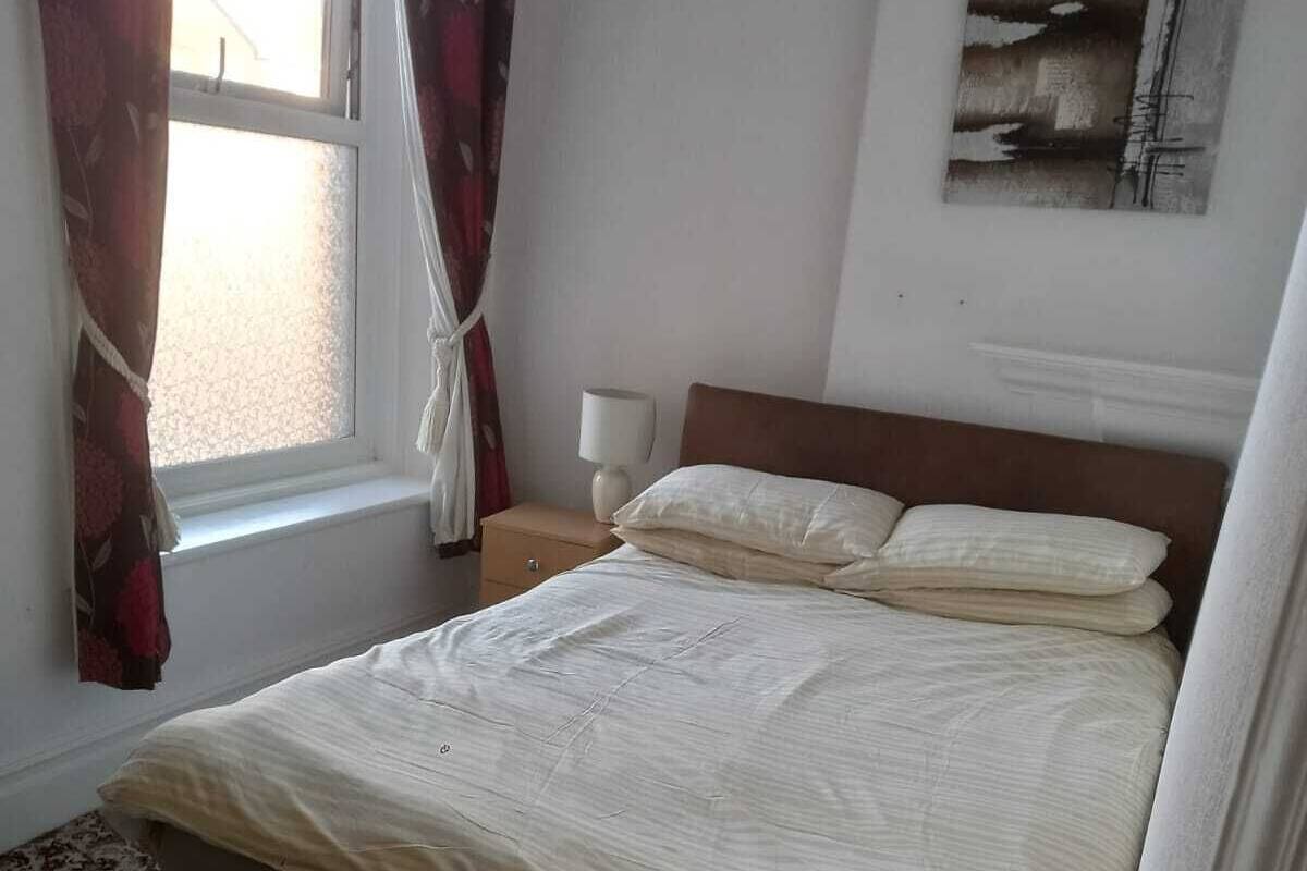 A neatly made bed with a headboard, a bedside lamp, and a window with curtains.