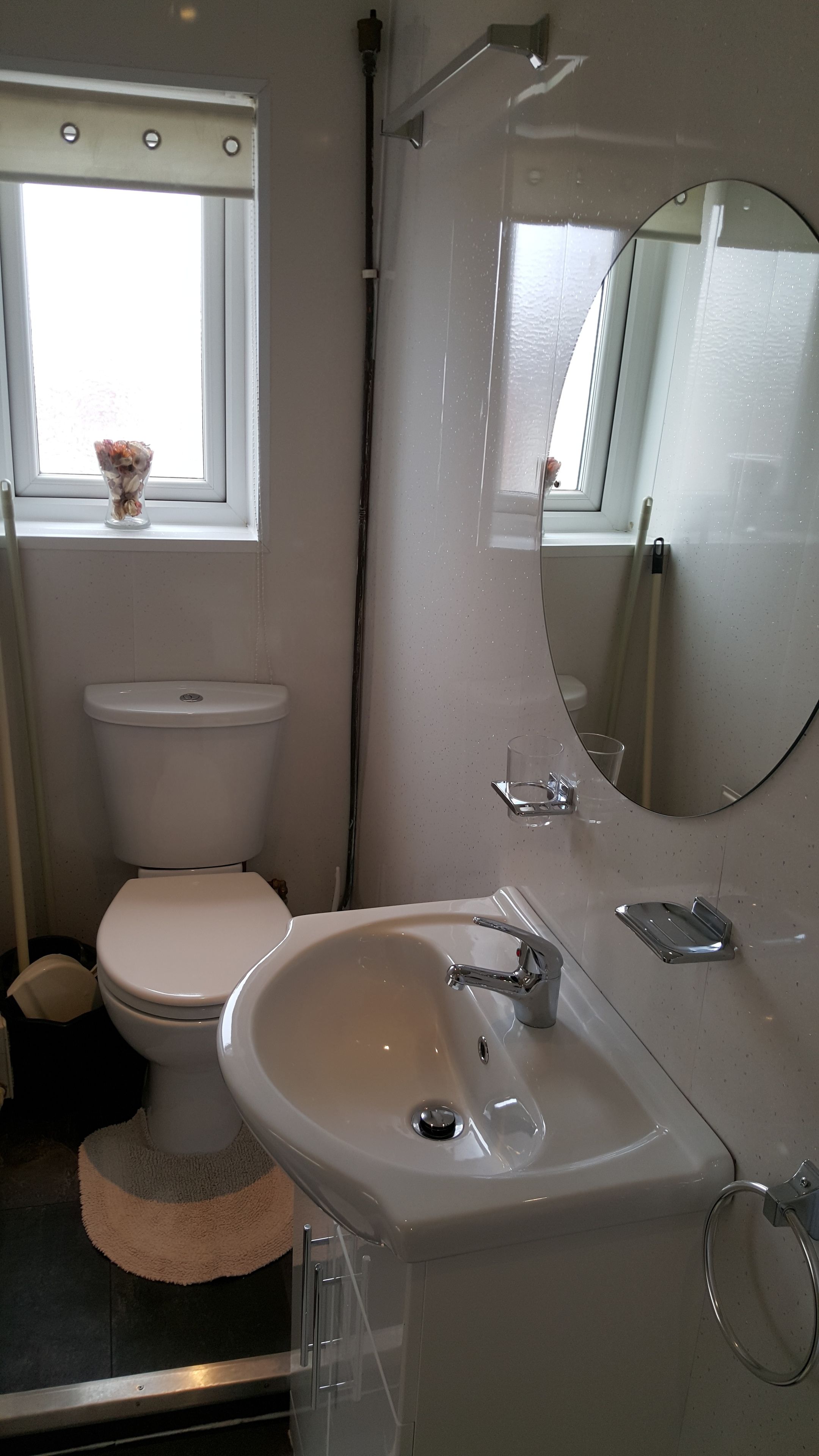A bathroom with a toilet, sink, and a window with a small vase.