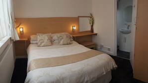 Een net opgemaakt bed met een bloemenbedekker, een nachtkastje met een lamp, en een spiegel erboven.