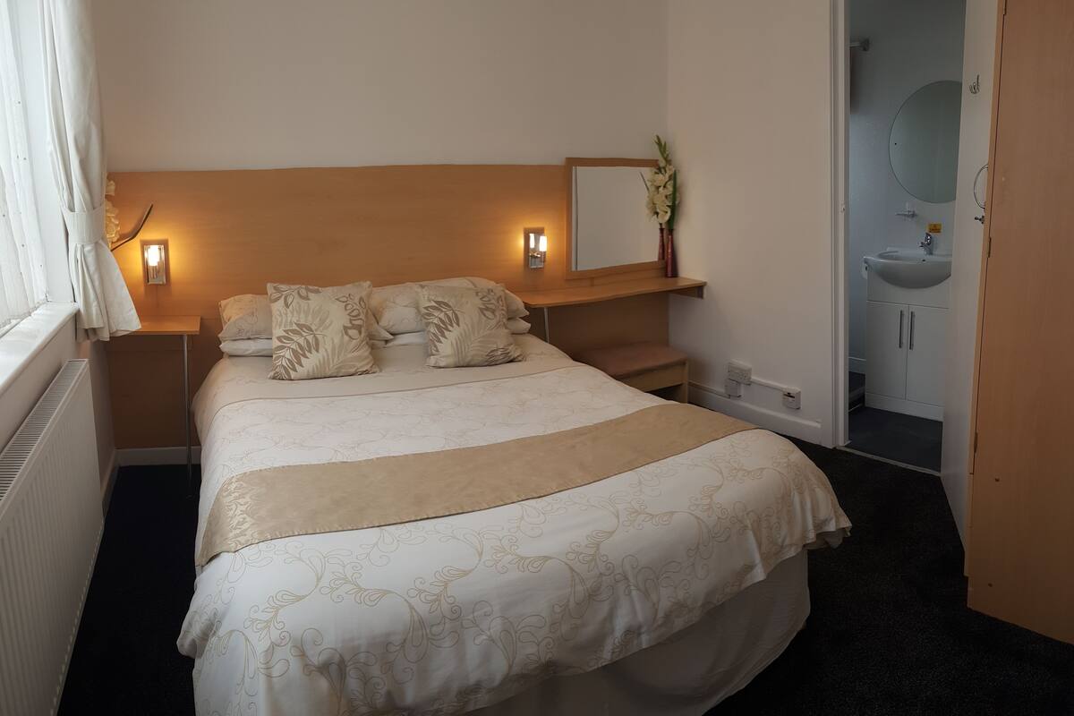 A neatly made bed with a floral bedspread, a bedside table with a lamp, and a mirror above it.