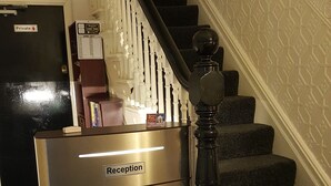 Een receptiebalie met een bordje met de tekst 'Receptie' en een trap met een zwarte balustrade.