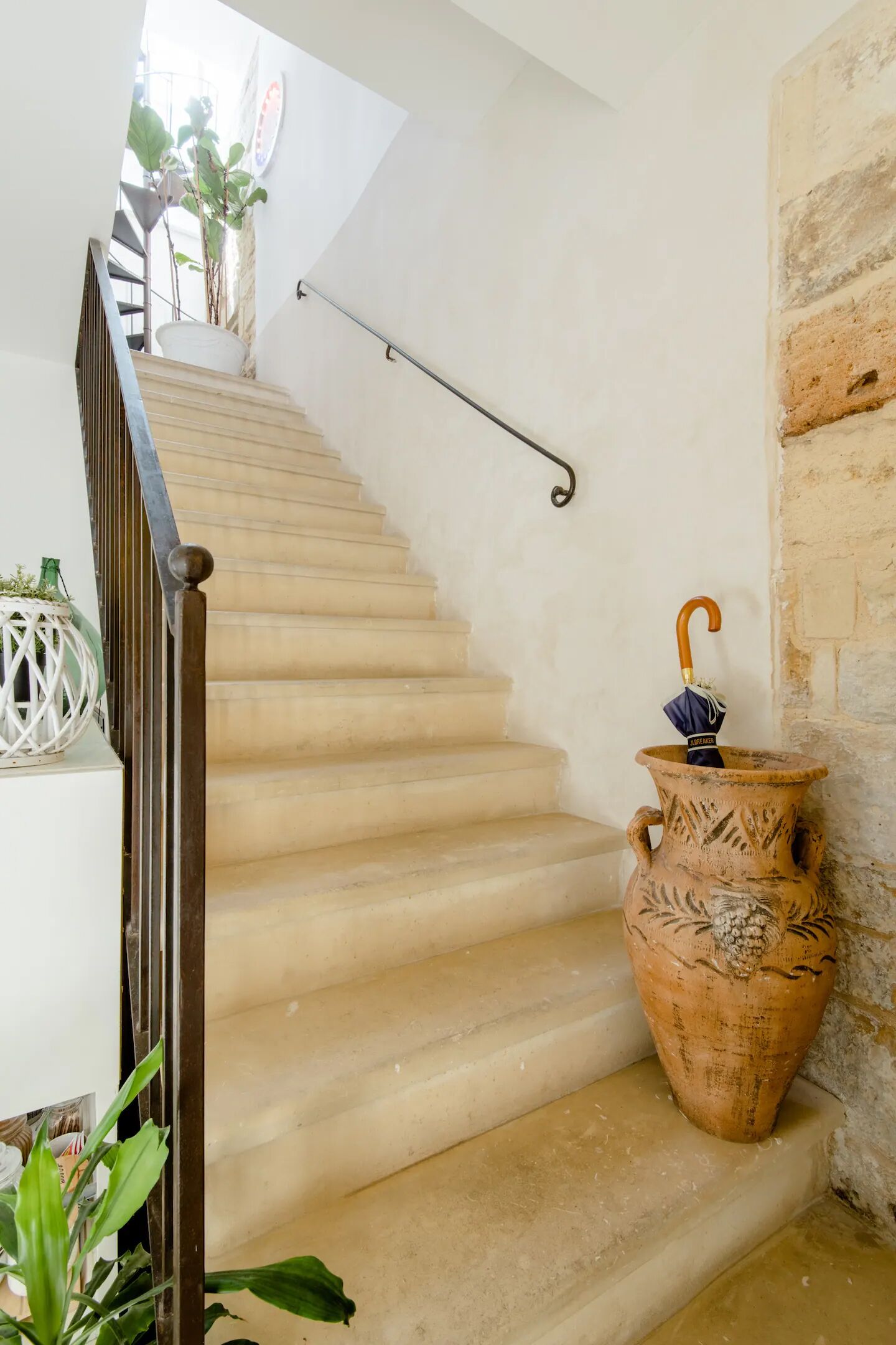 Un escalier avec une rampe métallique, une plante en pot et un pot en terre cuite contenant un parapluie.