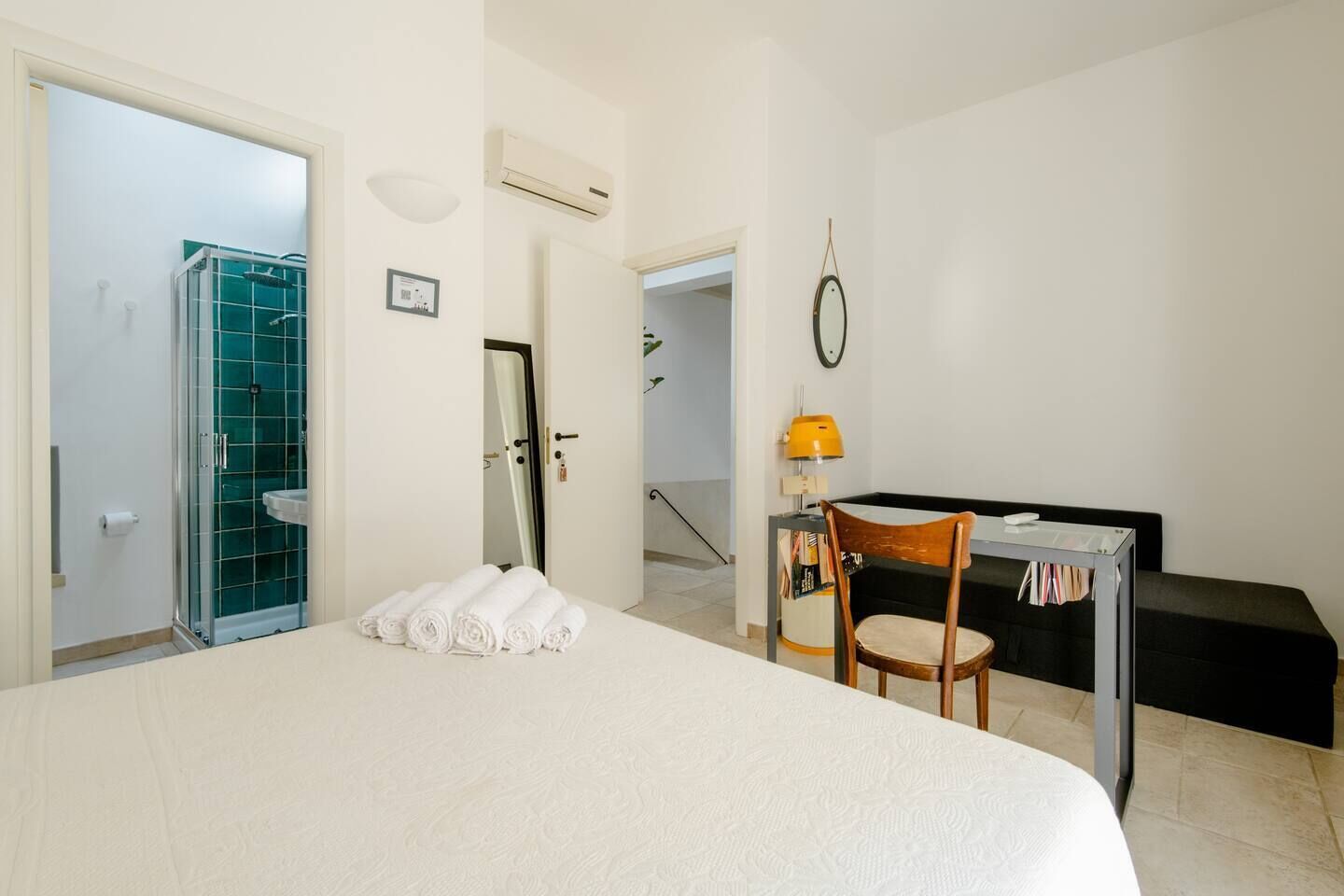 Une chambre d’hôtel avec un grand lit, un bureau avec une chaise, une petite table avec une lampe et un espace douche.