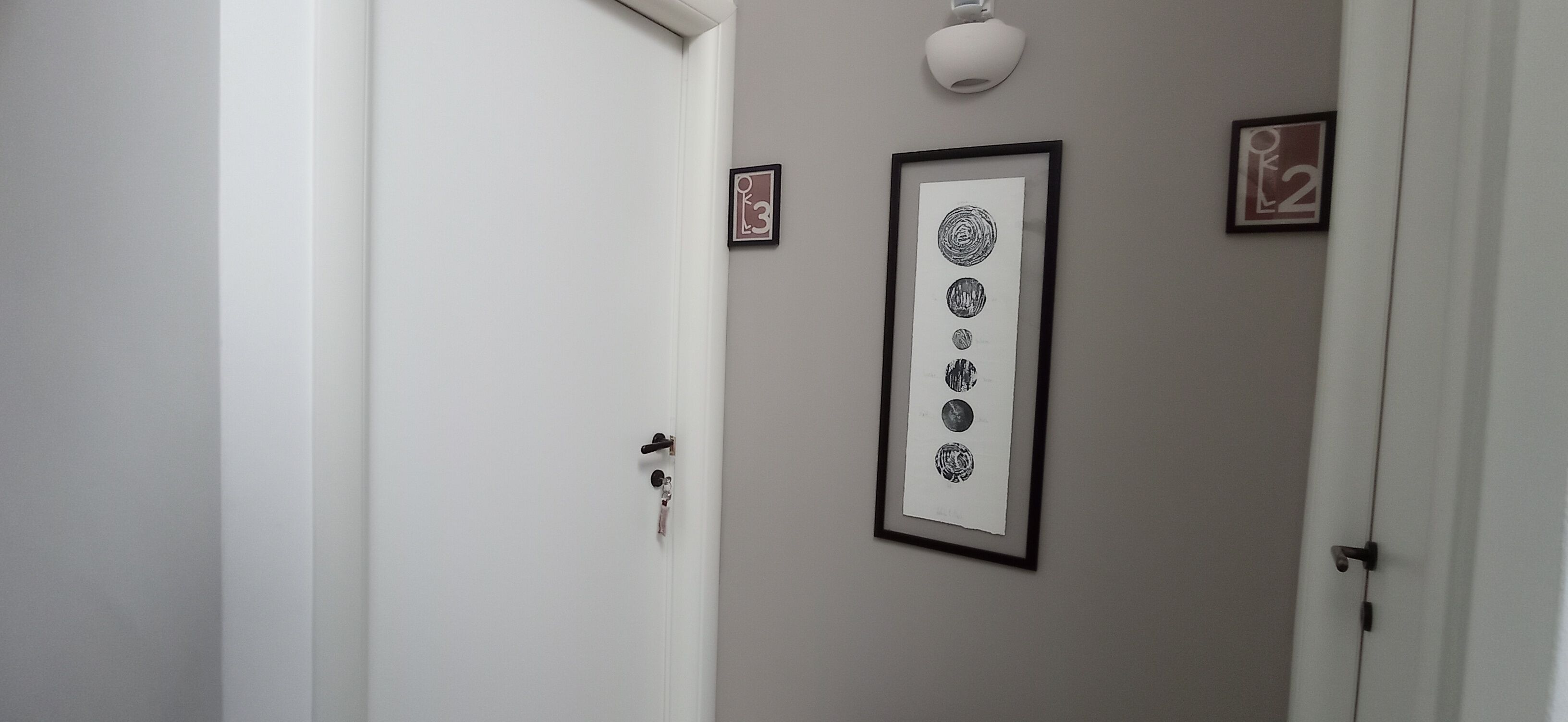 A hallway with a door, a framed artwork, and a wall-mounted light fixture.