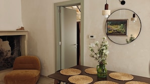 Un comedor con una mesa de madera, individuales tejidos, sillas de mimbre, un jarrón verde con flores y un cuadro en la pared.