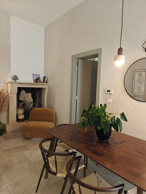 A dining area with a wooden table, chairs, a potted plant, a fireplace, and a mirror on the wall.