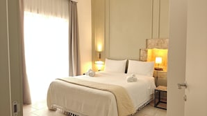 Habitación de hotel con cama, dos lámparas de noche, una mesita y vistas al exterior a través de una ventana con cortinas.