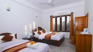 A hotel room with two beds, a wooden cabinet, a nightstand, a ceiling fan, and a window with curtains. - Chitwan Park Village (Sauraha)