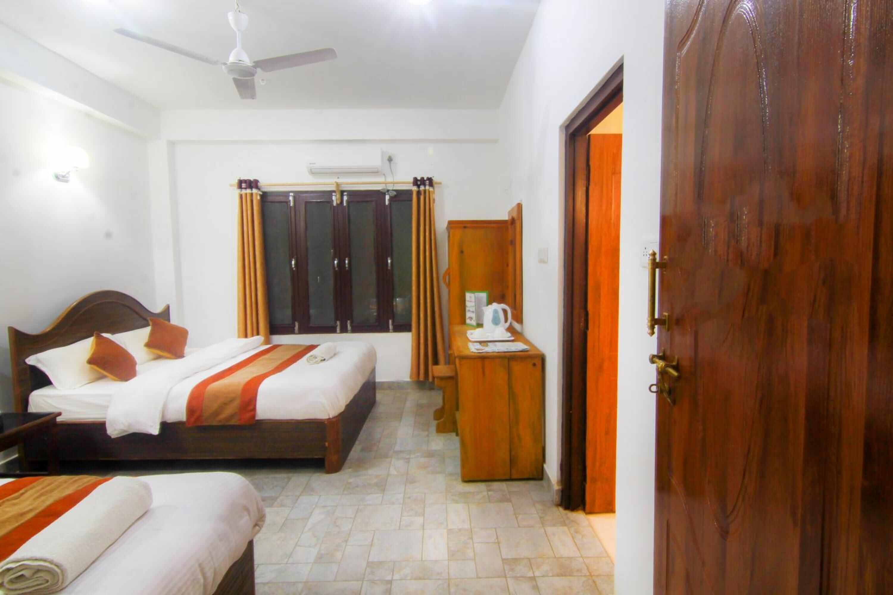A hotel room with two beds, a desk, a wardrobe, and a door.