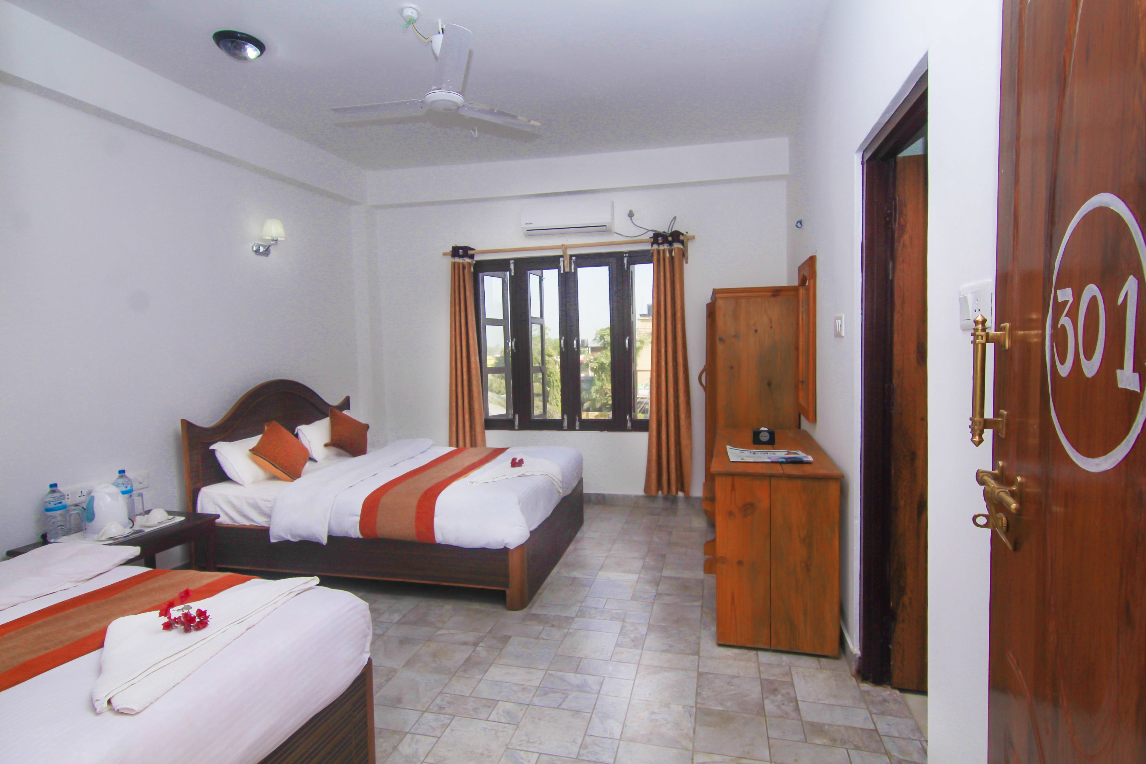 A hotel room with two beds, a wardrobe, a desk, and a door with a number.