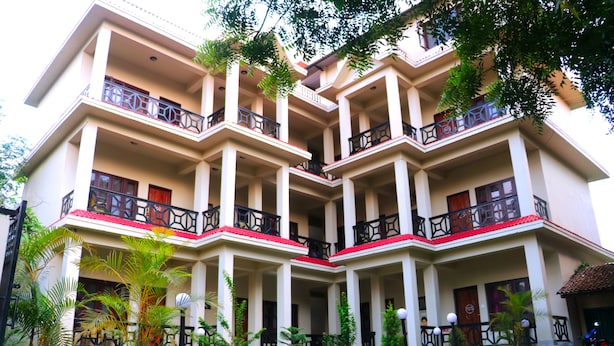 A multi-story hotel with balconies, a stone wall in front, and tropical plants. - Chitwan Park Village (Sauraha)