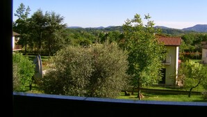Vista de una casa con tejado de tejas rojas, rodeada de vegetación y montañas al fondo.