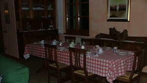 Un comedor con una mesa dispuesta para cuatro personas, sillas de madera, un aparador con puertas de cristal y una ventana con cortinas.
