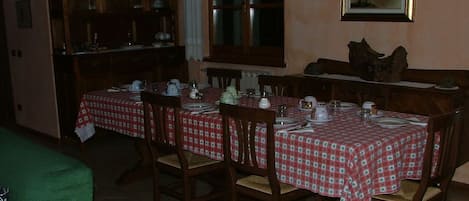 A dining area with a table set for four, wooden chairs, a cabinet with glass doors, and a window with curtains.